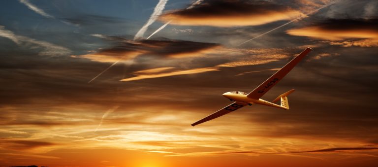 Glider flying under sunset clouds