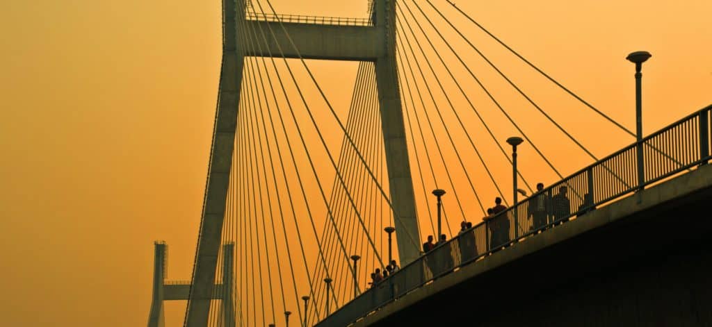 people walking across a suspension bridge at sunset